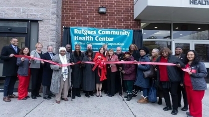 Image of twenty people standing behind a red ribbon for the Rutgers Community Health Center
