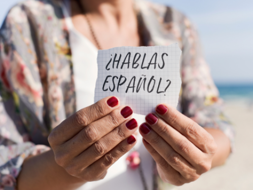 Image of a woman holding a card that reads, "Hablas Espanol?"